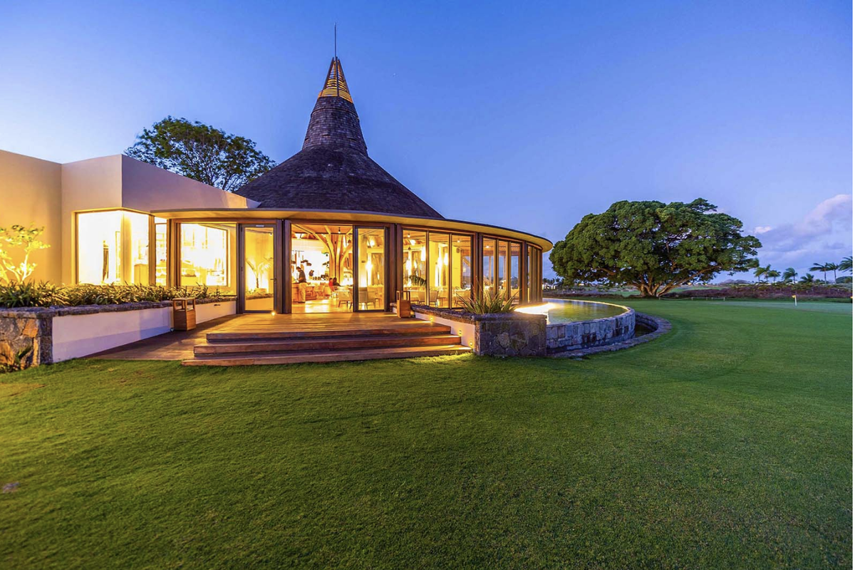 A stunning architectural exterior view of a circular building with a conical roof, featuring expansive glass walls, timber decking, and a landscaped garden setting.