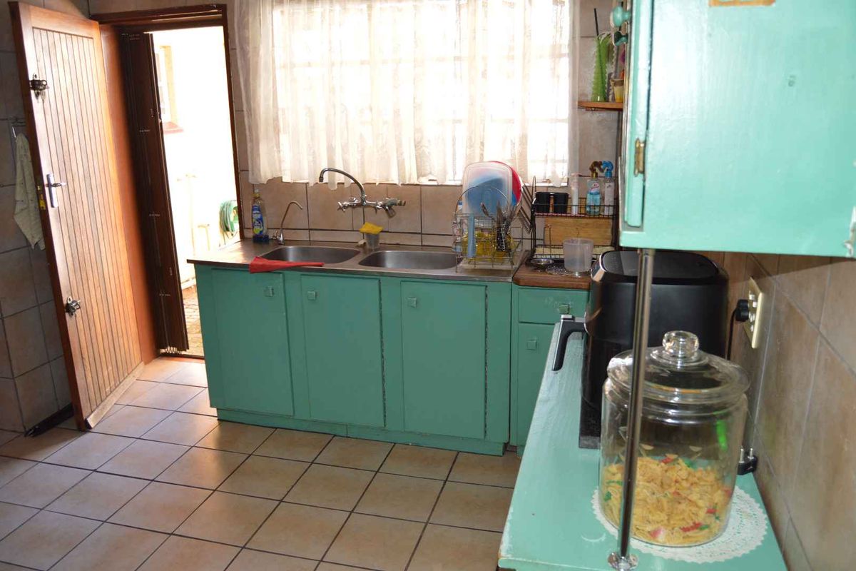 A dated kitchen featuring tiled flooring, a double basin sink, and painted cabinetry with direct access to the exterior.