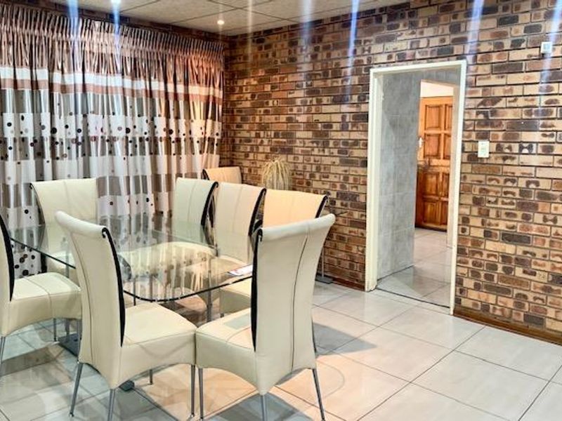 Dining area featuring an exposed brick feature wall, ceramic tiled flooring, and recessed ceiling lighting, providing a functional space for family meals.