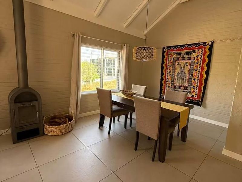 Dining area featuring a vaulted ceiling with exposed beams, tiled flooring, and a modern freestanding fireplace.