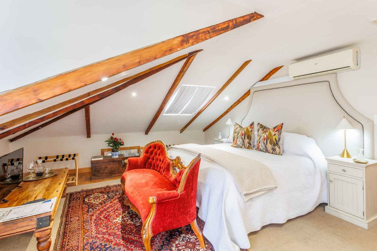 A charming attic-style bedroom featuring exposed timber rafters, a skylight, and a wall-mounted air conditioning unit.