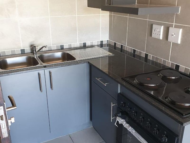 A compact, modern kitchen featuring grey cabinetry, granite countertops, a built-in oven with electric hob, and a double bowl stainless steel sink.