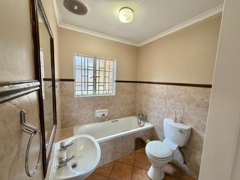 A functional bathroom featuring a bathtub, pedestal basin, and toilet, with neutral wall tiles and tiled flooring.
