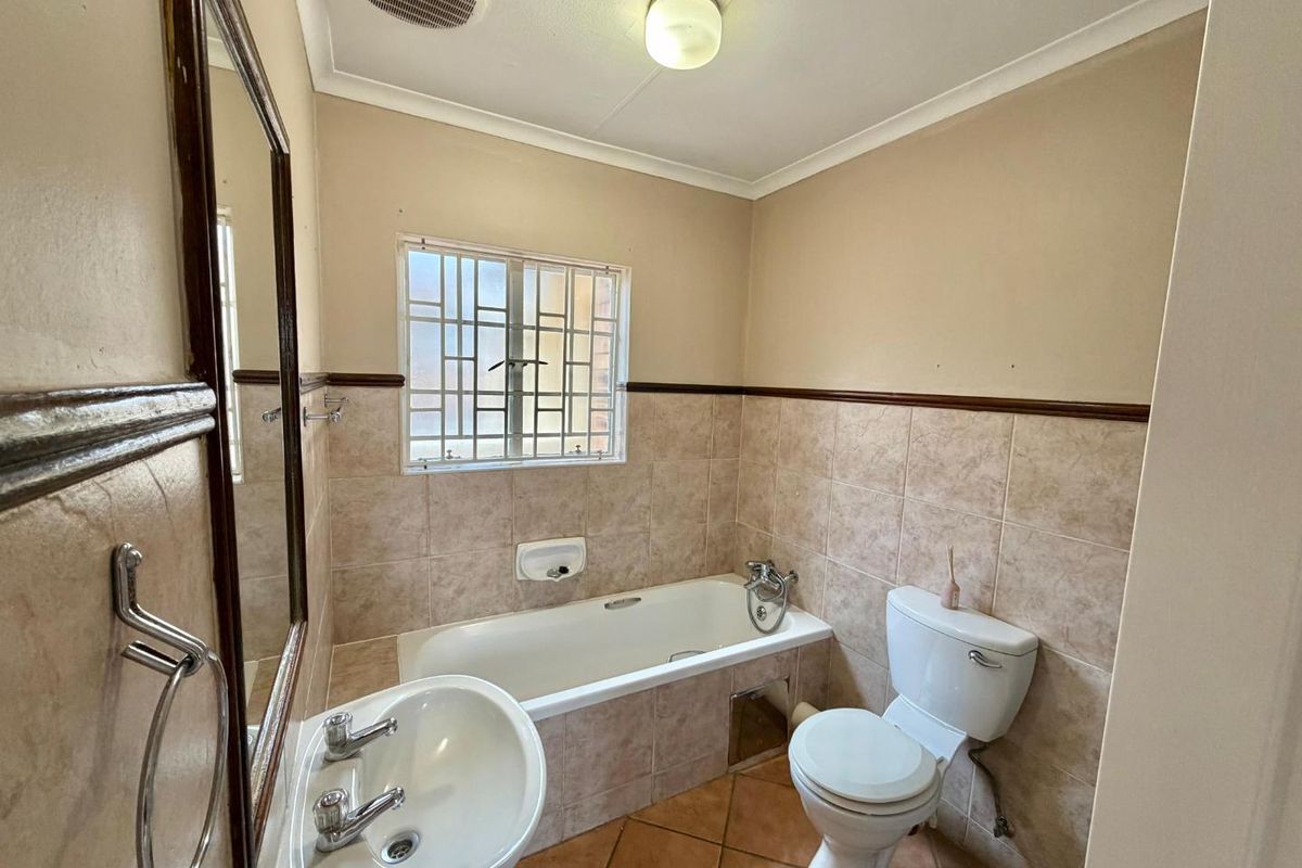 A functional bathroom featuring a bathtub, pedestal basin, and toilet, with neutral wall tiles and tiled flooring.