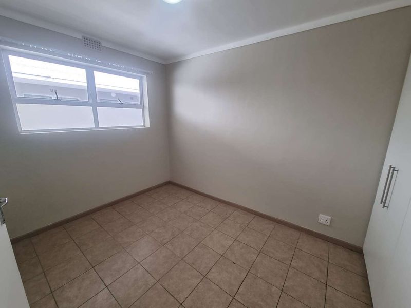 A clean, empty bedroom featuring neutral wall paint, tiled flooring, and built-in storage cupboards.