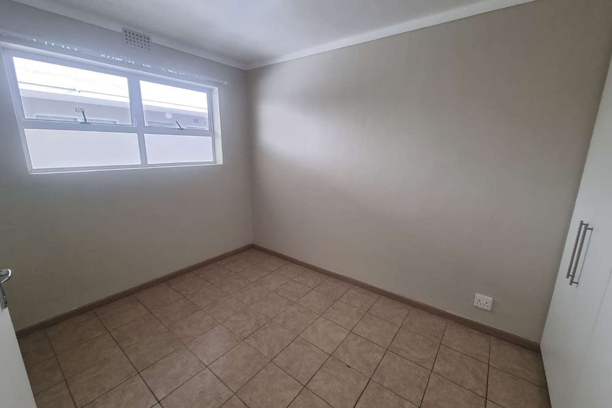 A clean, empty bedroom featuring neutral wall paint, tiled flooring, and built-in storage cupboards.