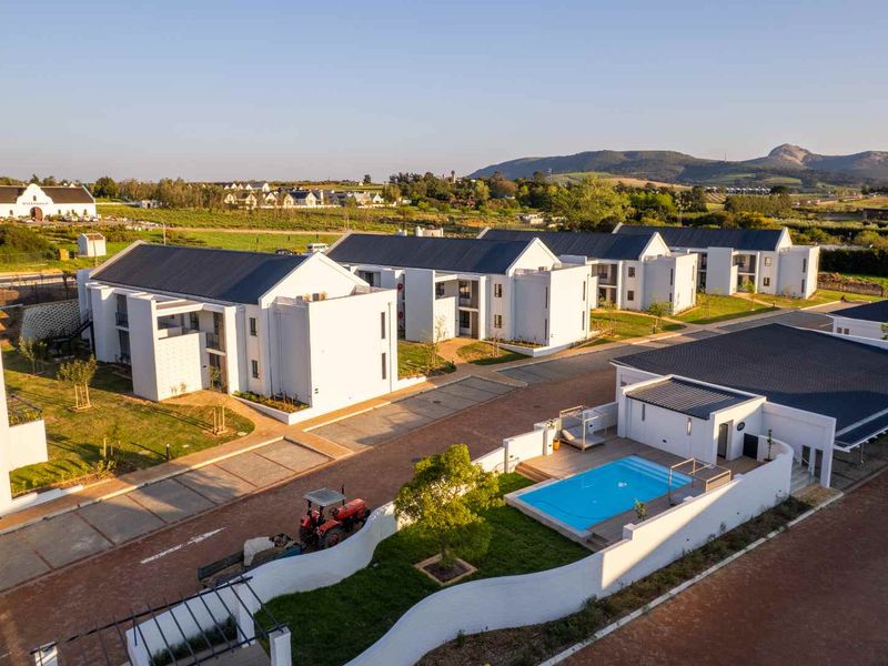 Aerial view of a modern residential apartment complex featuring white buildings with dark pitched roofs, a communal swimming pool, and landscaped grounds.