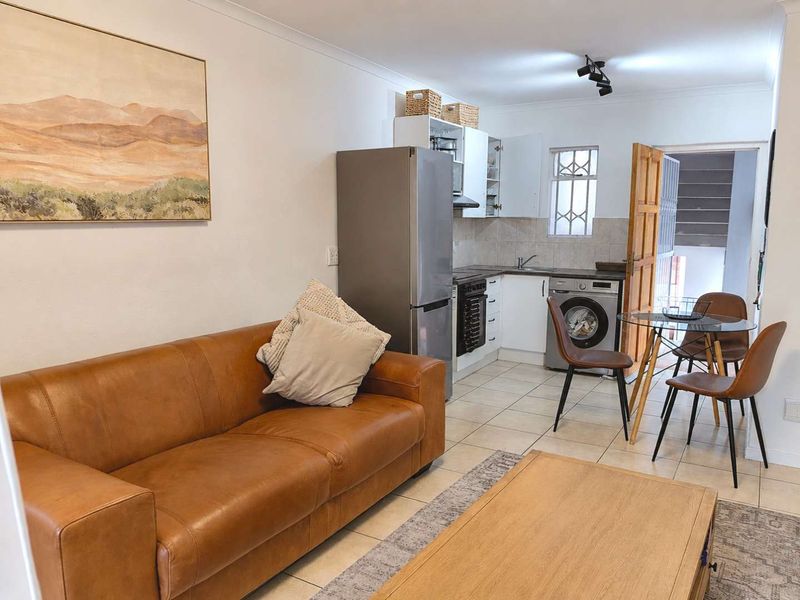 Open-plan living and kitchen area featuring tiled flooring, compact cabinetry, and direct access to the exterior via a security door.