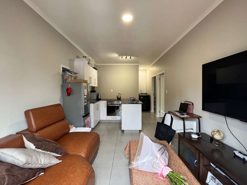Open-plan living area featuring a modern kitchen with built-in cabinetry, oven, and hob, seamlessly flowing into the lounge space with tiled flooring throughout.