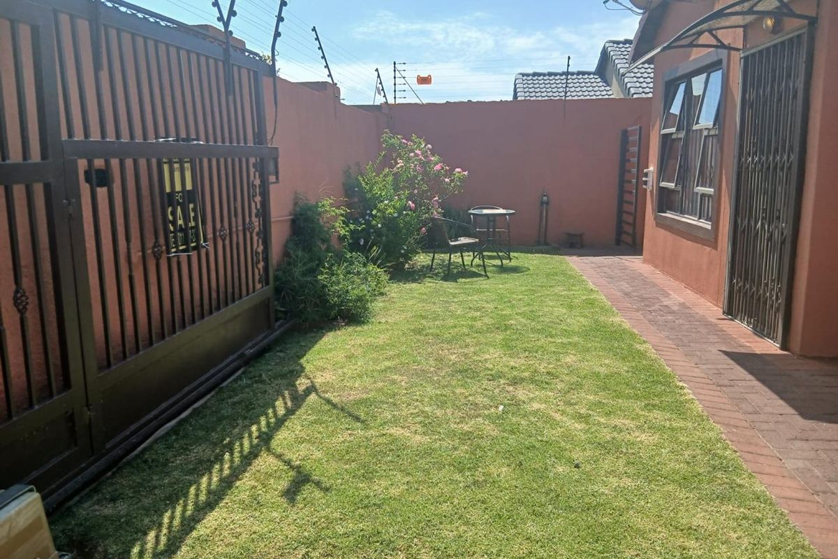 A private rear garden area featuring a paved walkway, lawn, and secure perimeter walling with electric fencing.