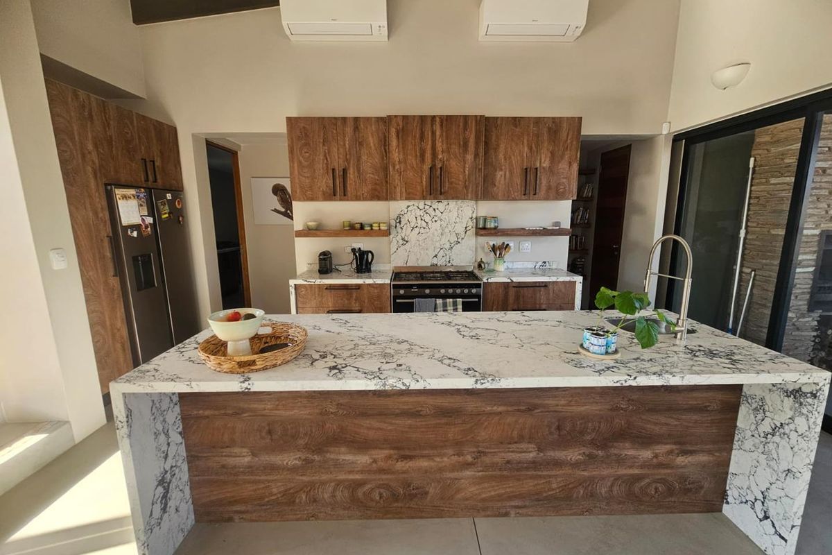 Modern kitchen featuring a large marble-topped island, wood-grain cabinetry, built-in gas stove, and dual wall-mounted air conditioning units.