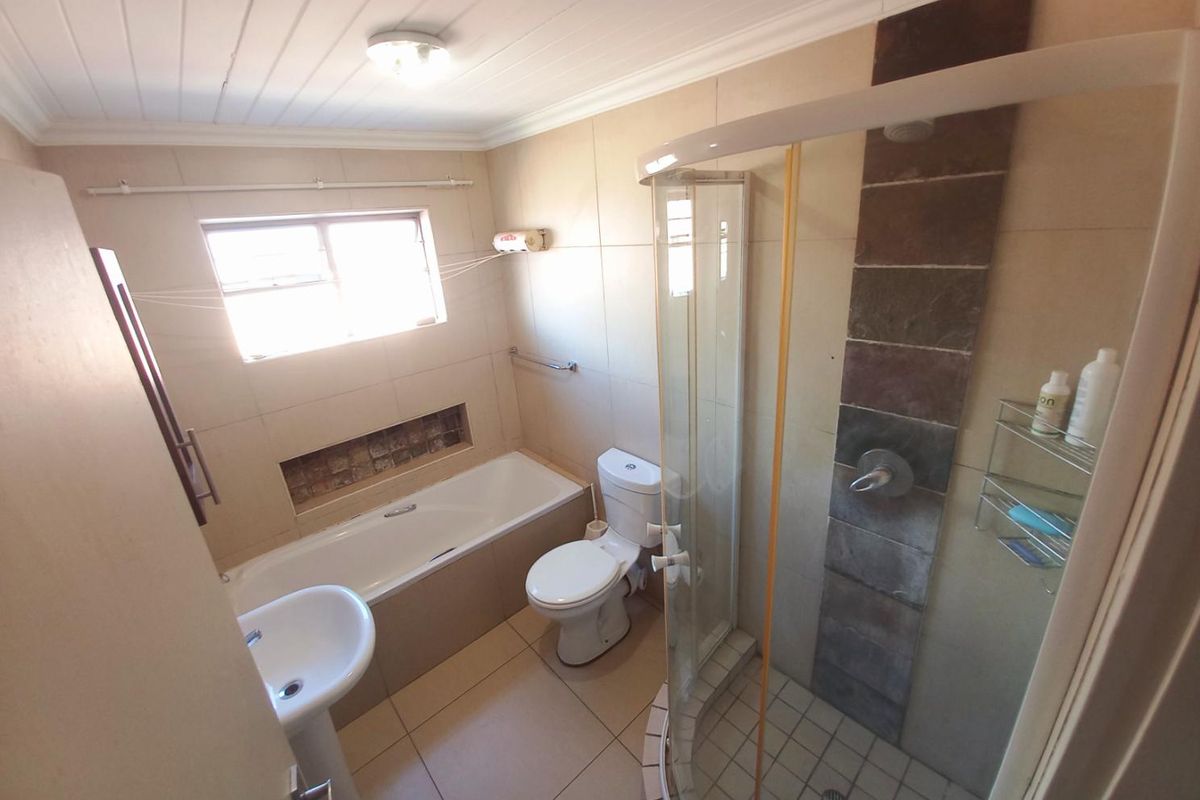 A functional bathroom featuring a separate bathtub, a corner glass shower enclosure, a pedestal basin, and a toilet with neutral wall and floor tiling.