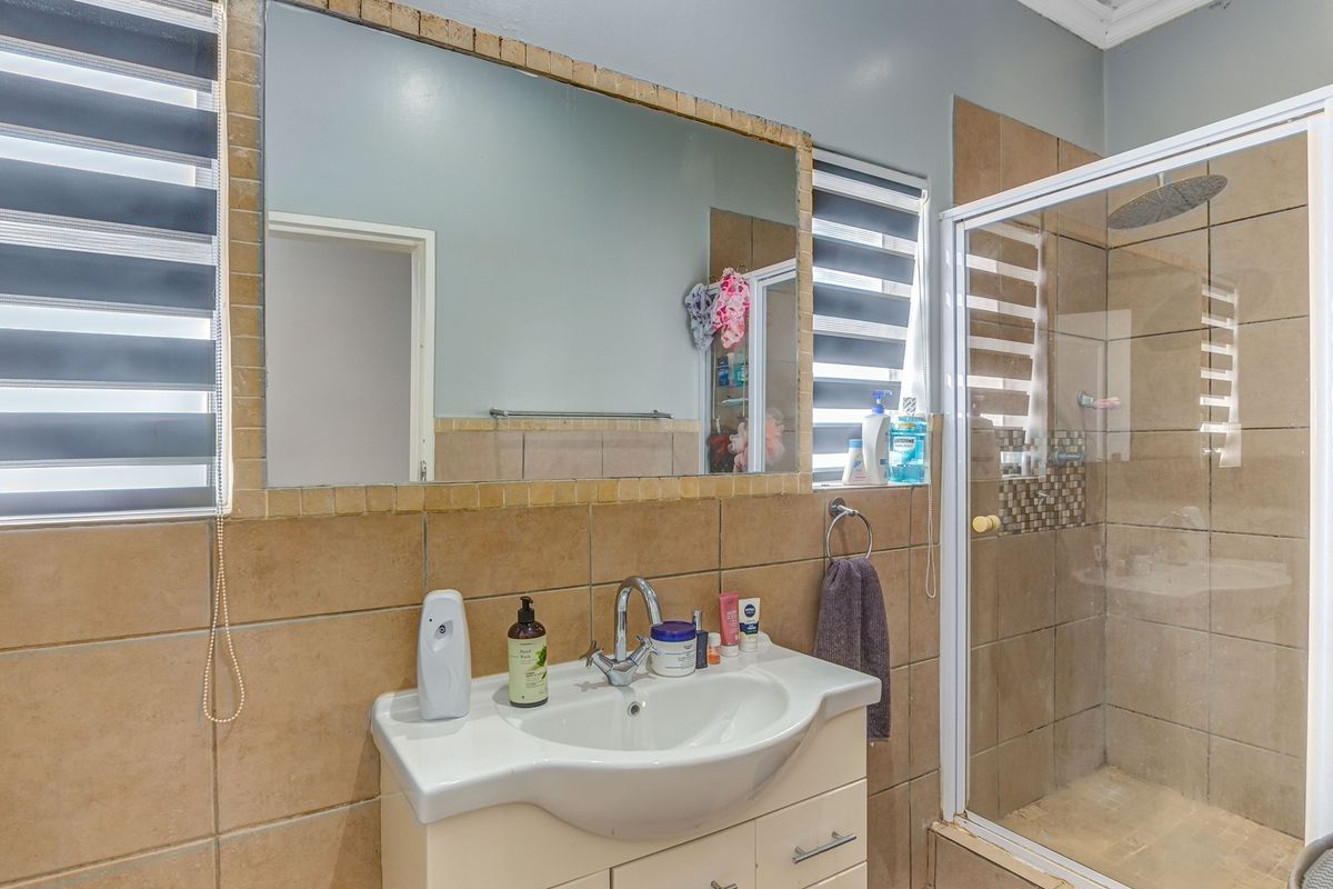 A well-maintained bathroom featuring a vanity unit with basin, a large wall mirror, and a tiled shower enclosure with a modern rain shower head.