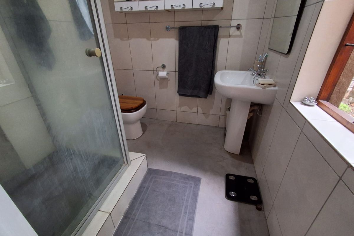 A functional bathroom featuring a pedestal basin, toilet, and a glass-enclosed shower with neutral wall tiling.