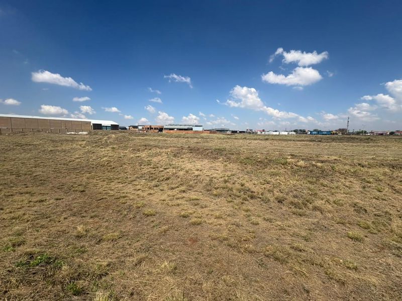 A wide-angle view of a vacant commercial land plot with surrounding industrial development visible in the distance.