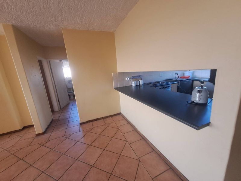 Open plan living area featuring a kitchen pass-through counter, tiled flooring, and direct access to the hallway and bathroom.