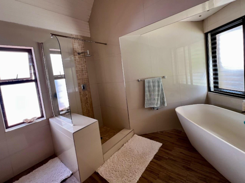 Modern bathroom featuring a freestanding bathtub, a walk-in shower with glass screen, neutral wall tiling, and wood-look flooring.