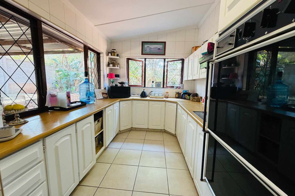 A functional kitchen featuring white cabinetry, laminate countertops, tiled flooring, and a built-in oven, with large windows providing natural light and garden views.