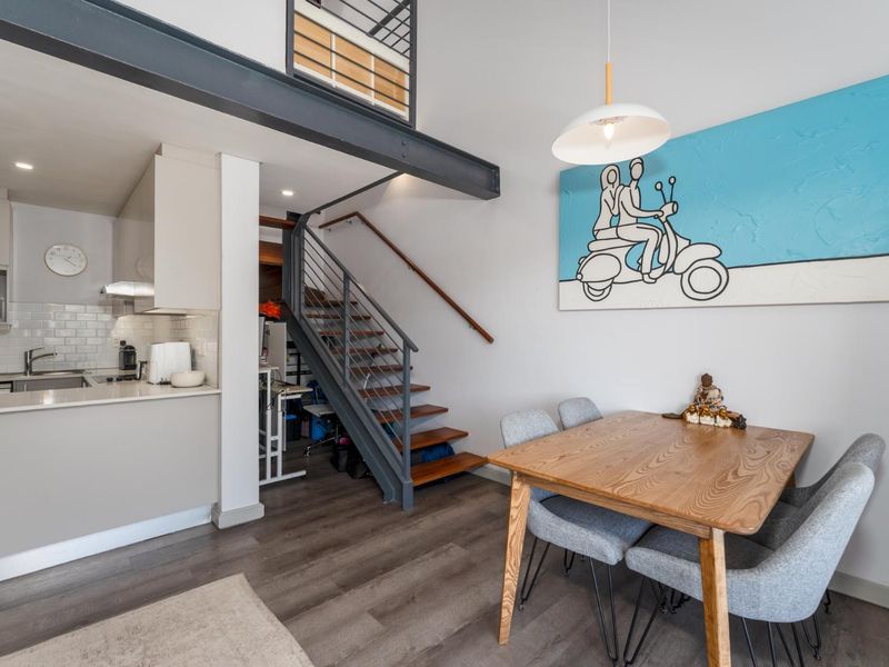 Modern open-plan living area featuring a compact kitchen with subway tile backsplash, a striking staircase with metal railings, and a mezzanine level.
