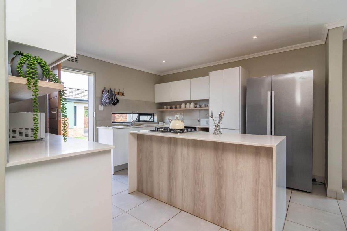 Modern kitchen featuring a central island with a gas hob, sleek white cabinetry, stone countertops, and direct access to the exterior.