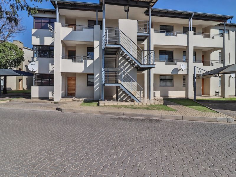Front elevation of a multi-story townhouse complex featuring external metal staircases, private balconies, and paved parking areas with carports.
