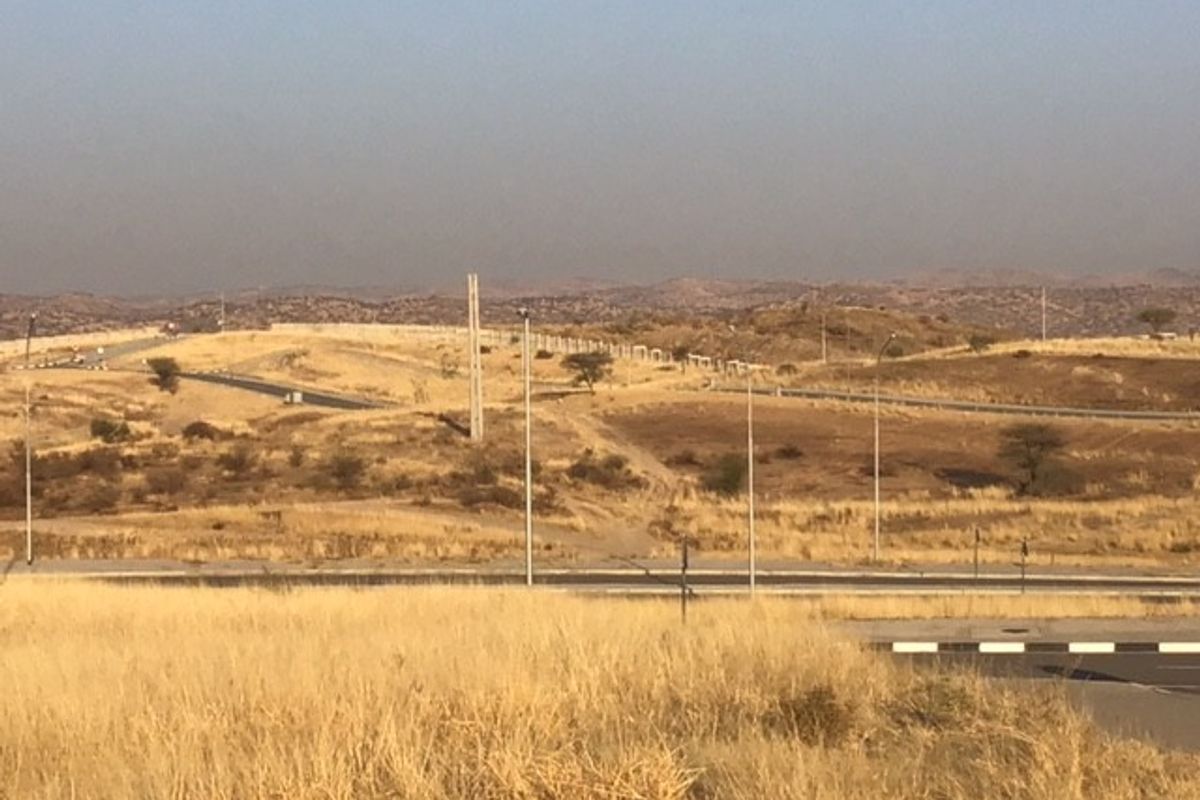 An elevated view of a vacant commercial land plot featuring paved road access, street lighting infrastructure, and surrounding hilly landscape.