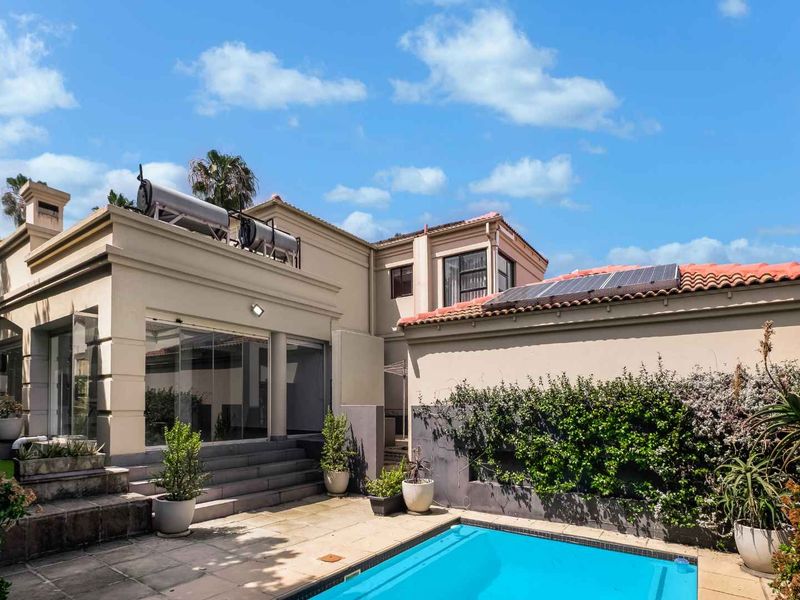 Rear exterior view featuring a swimming pool, paved patio area, solar water heating system, and solar panels on the roof.
