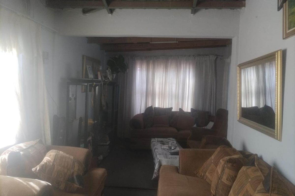 A living room featuring exposed timber ceiling beams and large windows, offering a traditional layout with potential for modernization.