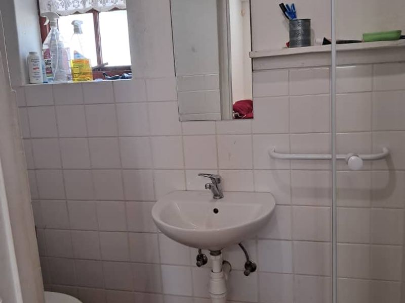 A functional bathroom featuring a wall-mounted basin, toilet, and glass shower screen with tiled finishes, requiring some cosmetic updates.