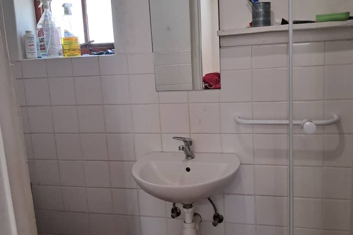 A functional bathroom featuring a wall-mounted basin, toilet, and glass shower screen with tiled finishes, requiring some cosmetic updates.