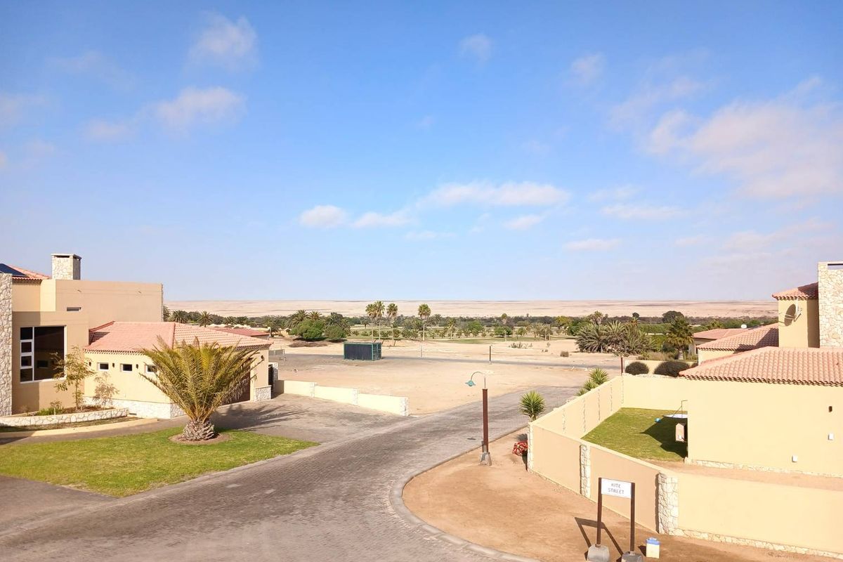 An elevated aerial view of a residential estate featuring paved driveways, boundary walls, and tiled roof structures set against a desert landscape.