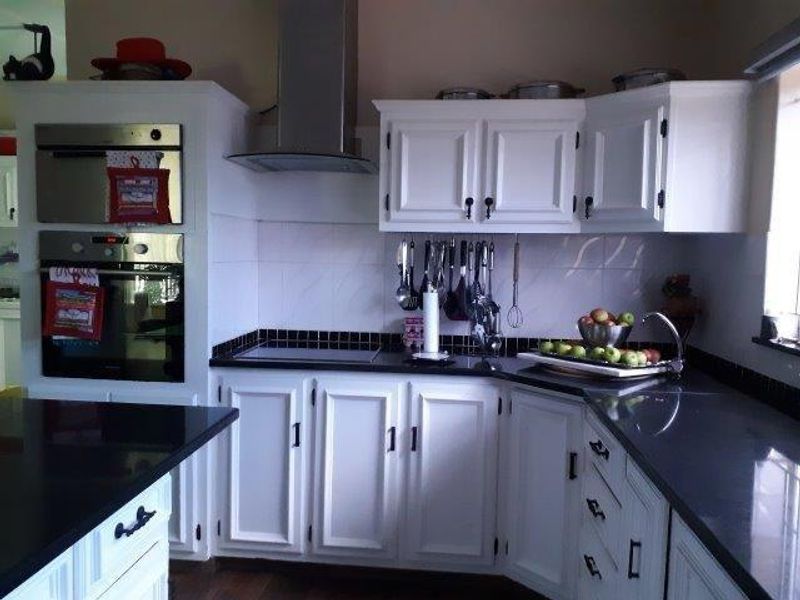 A functional kitchen featuring white cabinetry, black granite countertops, a built-in oven and microwave, and a stainless steel extractor fan.