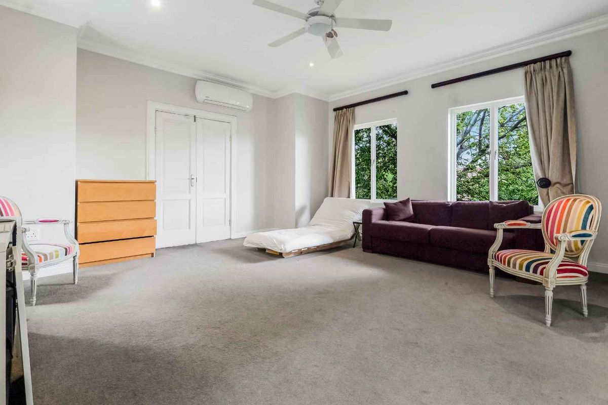 A spacious bedroom featuring neutral carpeting, a ceiling fan, and a wall-mounted air conditioning unit, with large windows providing natural light.
