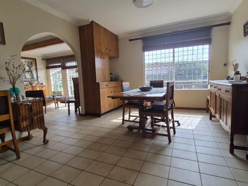 Open-plan living and dining area featuring tiled flooring, built-in wooden cabinetry, and an arched transition to an adjacent room with natural light.