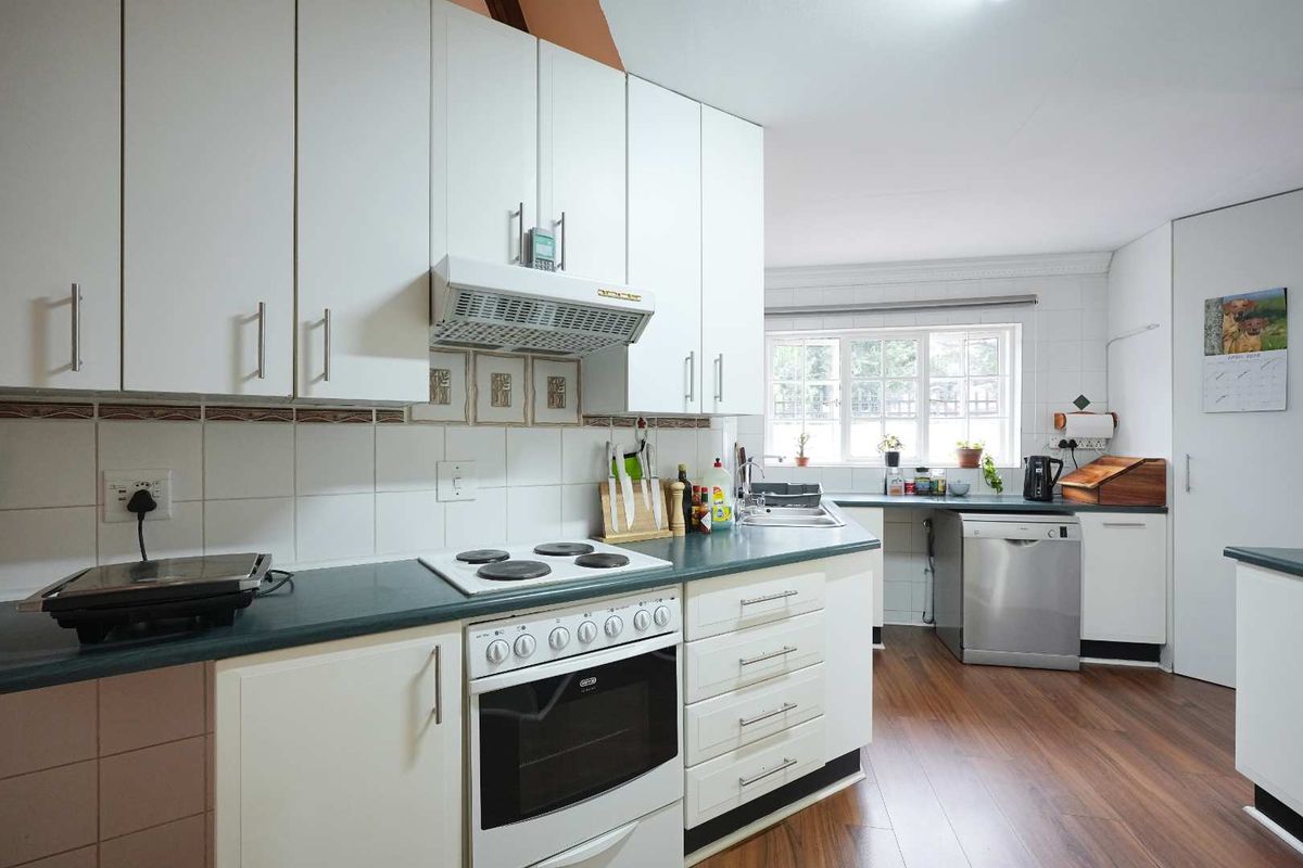 Functional kitchen featuring white cabinetry, dark countertops, built-in oven, electric hob, extractor fan, and stainless steel sink with tiled backsplash.