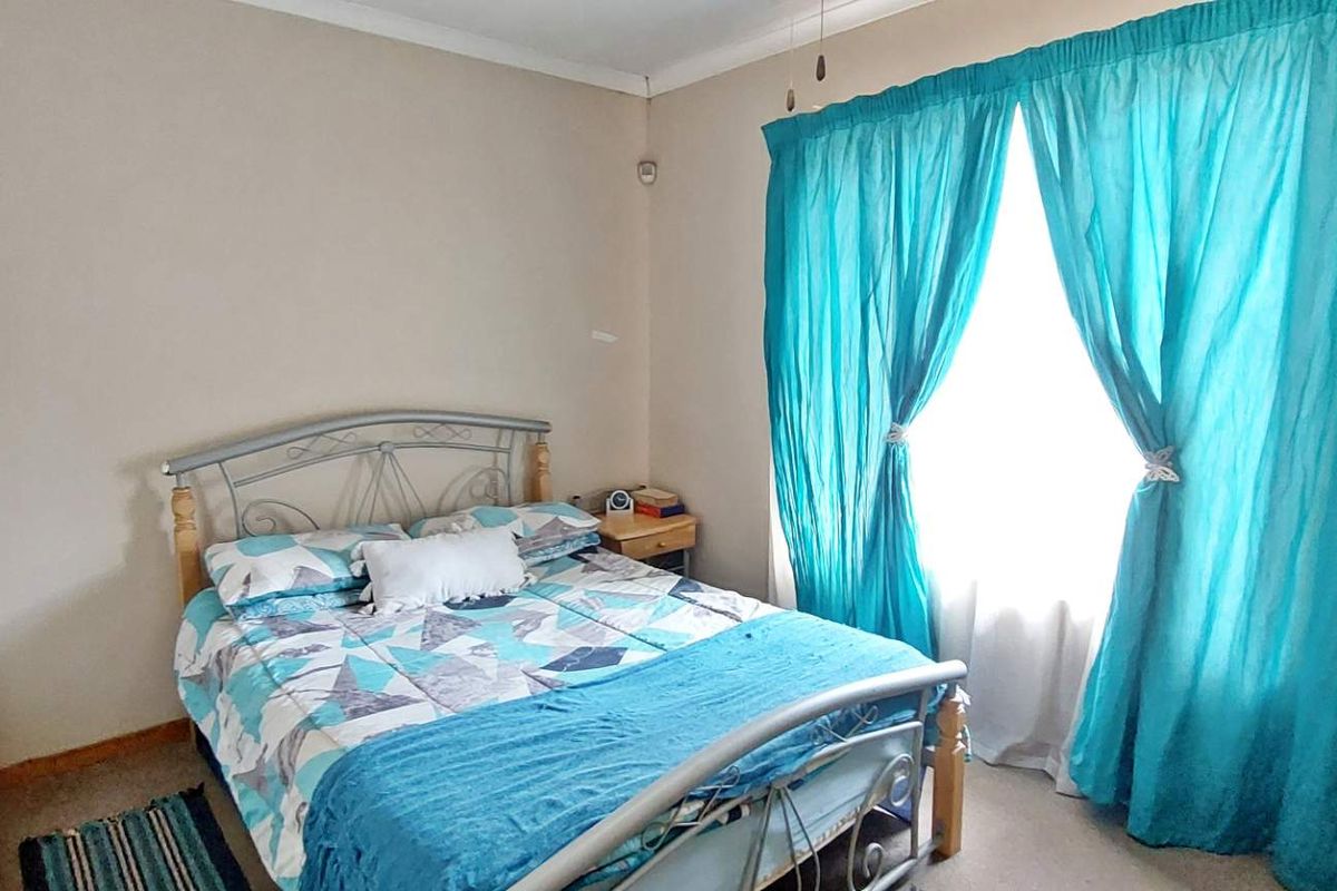 A standard bedroom featuring neutral wall tones, built-in cupboard space, and a window dressed with curtains.