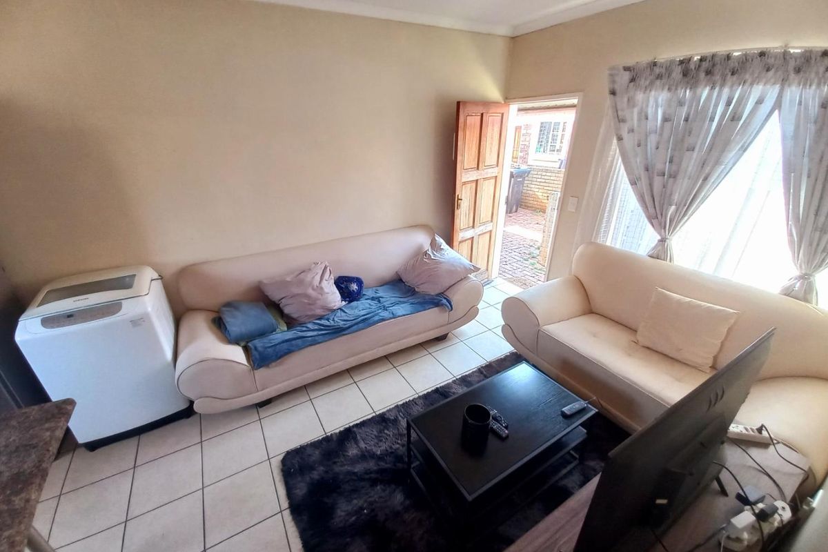A living room area featuring tiled flooring, a wooden exterior door, and a window with curtains, providing direct access to the outdoor space.