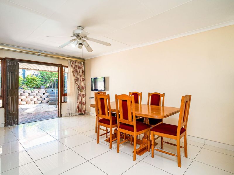 Bright dining area featuring white tiled flooring, a ceiling fan, and direct access to the rear patio through a sliding glass door.