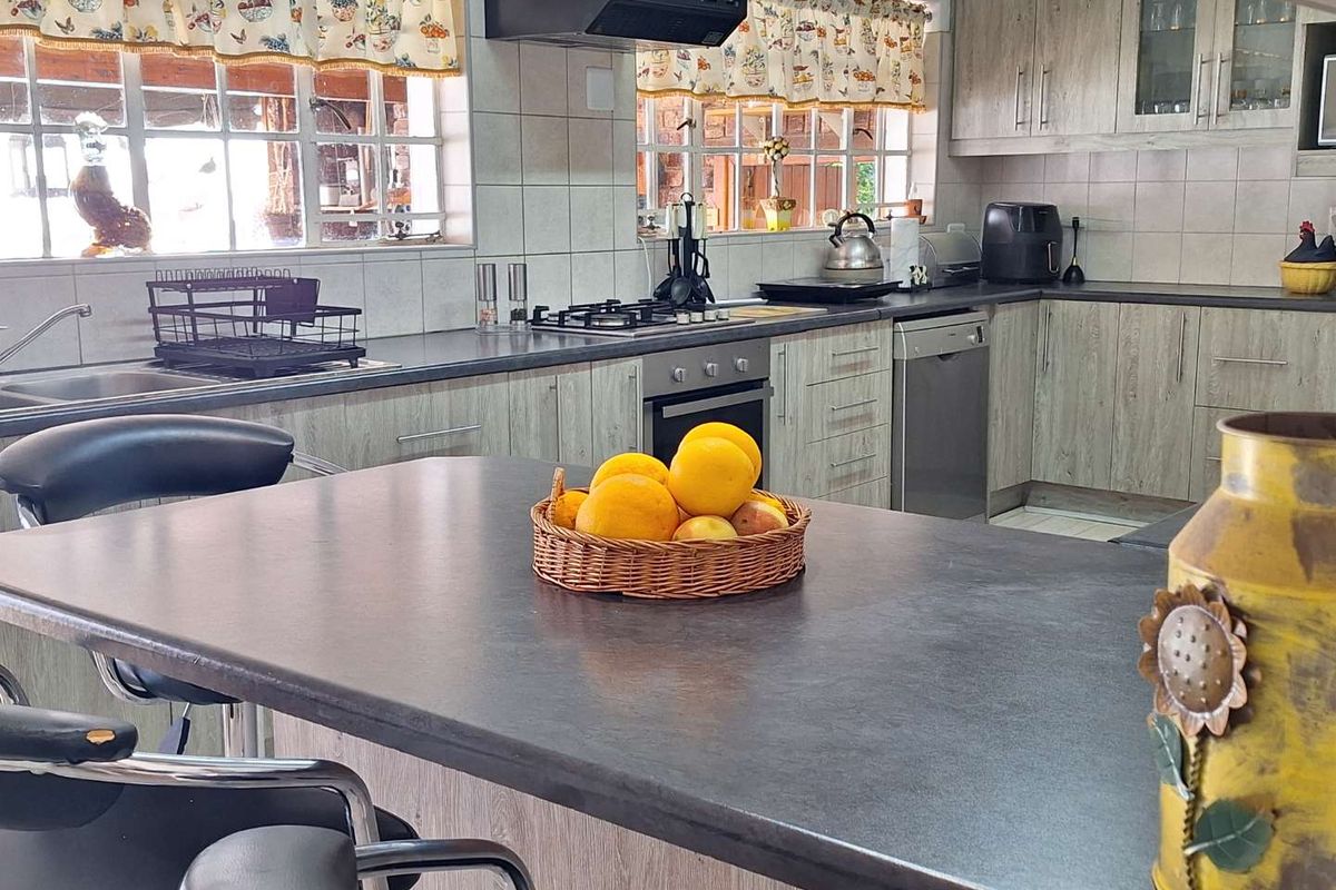 A functional kitchen featuring wood-look cabinetry, dark laminate countertops, a built-in oven, gas hob, extractor fan, and a central breakfast island.