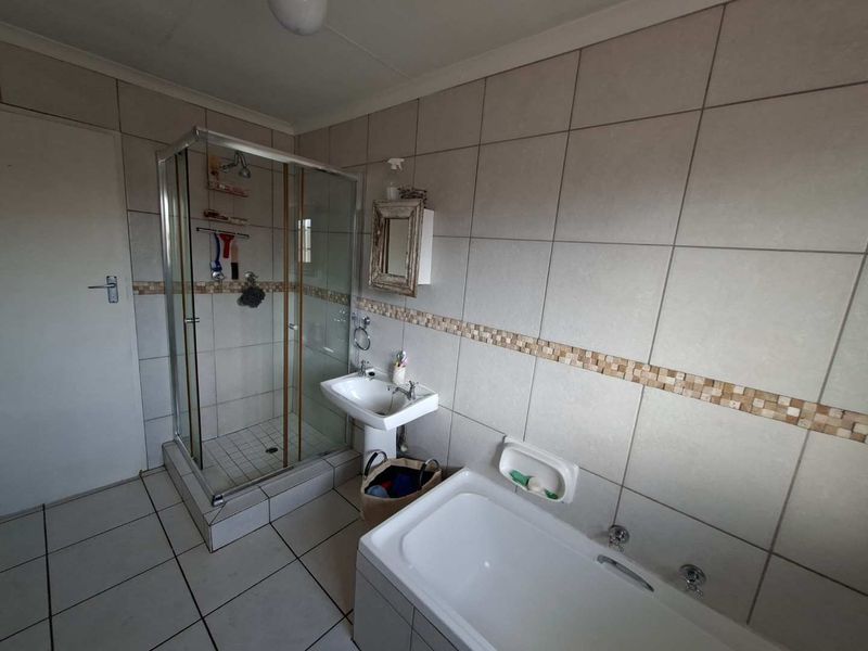 A functional bathroom featuring a shower enclosure, pedestal basin, and bathtub with neutral wall and floor tiling and a decorative mosaic border.