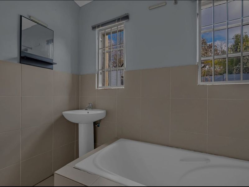 A functional bathroom featuring a pedestal basin, built-in bathtub, and neutral wall tiling, offering a clean canvas for potential modern updates.