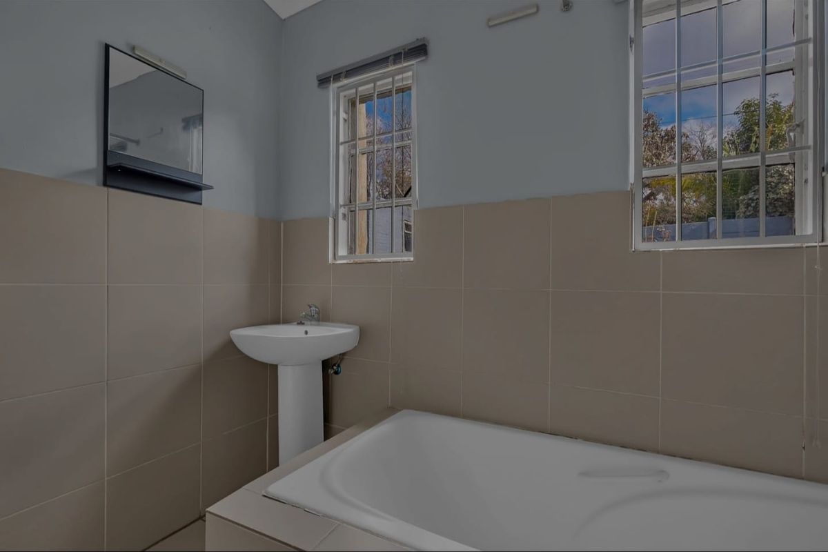 A functional bathroom featuring a pedestal basin, built-in bathtub, and neutral wall tiling, offering a clean canvas for potential modern updates.