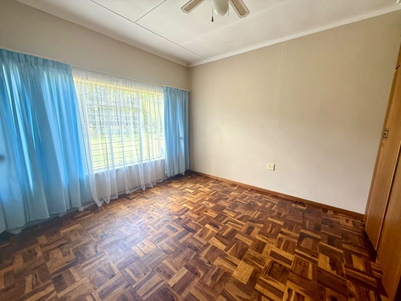 A vacant bedroom featuring classic parquet flooring, a ceiling fan, and built-in storage, offering a blank canvas for personalization.