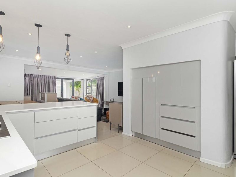 Modern open-plan kitchen and living area featuring sleek white cabinetry, stone countertops, integrated gas hob, and neutral tiled flooring throughout.