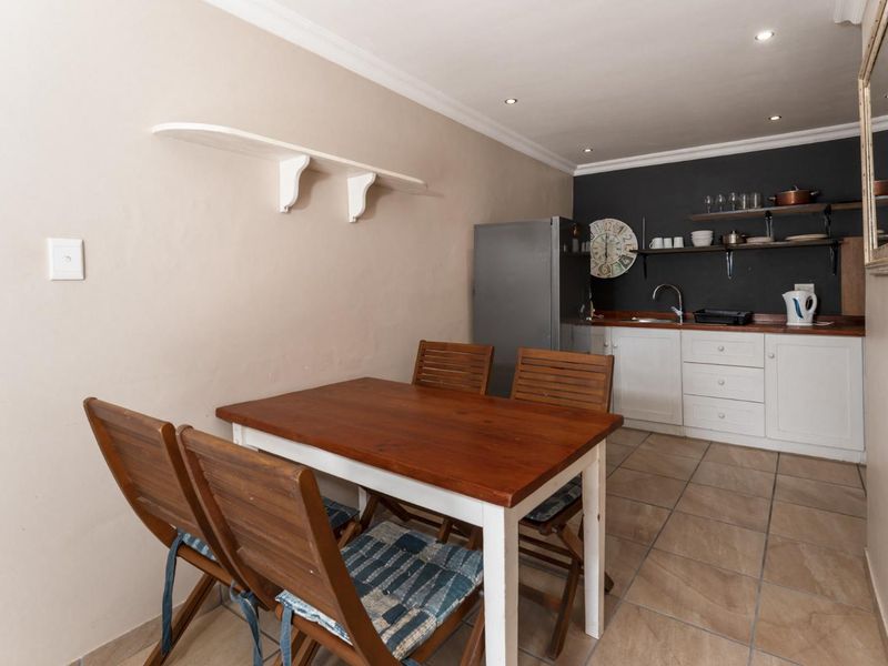 Open-plan kitchen and dining area featuring tiled flooring, white cabinetry, and wall-mounted shelving, providing a functional and compact living space.