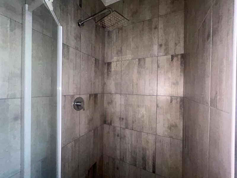 A modern shower enclosure featuring contemporary grey wall tiles and a square rainfall shower head.