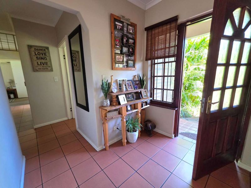 Welcoming entrance foyer featuring terracotta-style floor tiles, natural light from the timber-framed front door, and access to the interior hallway.