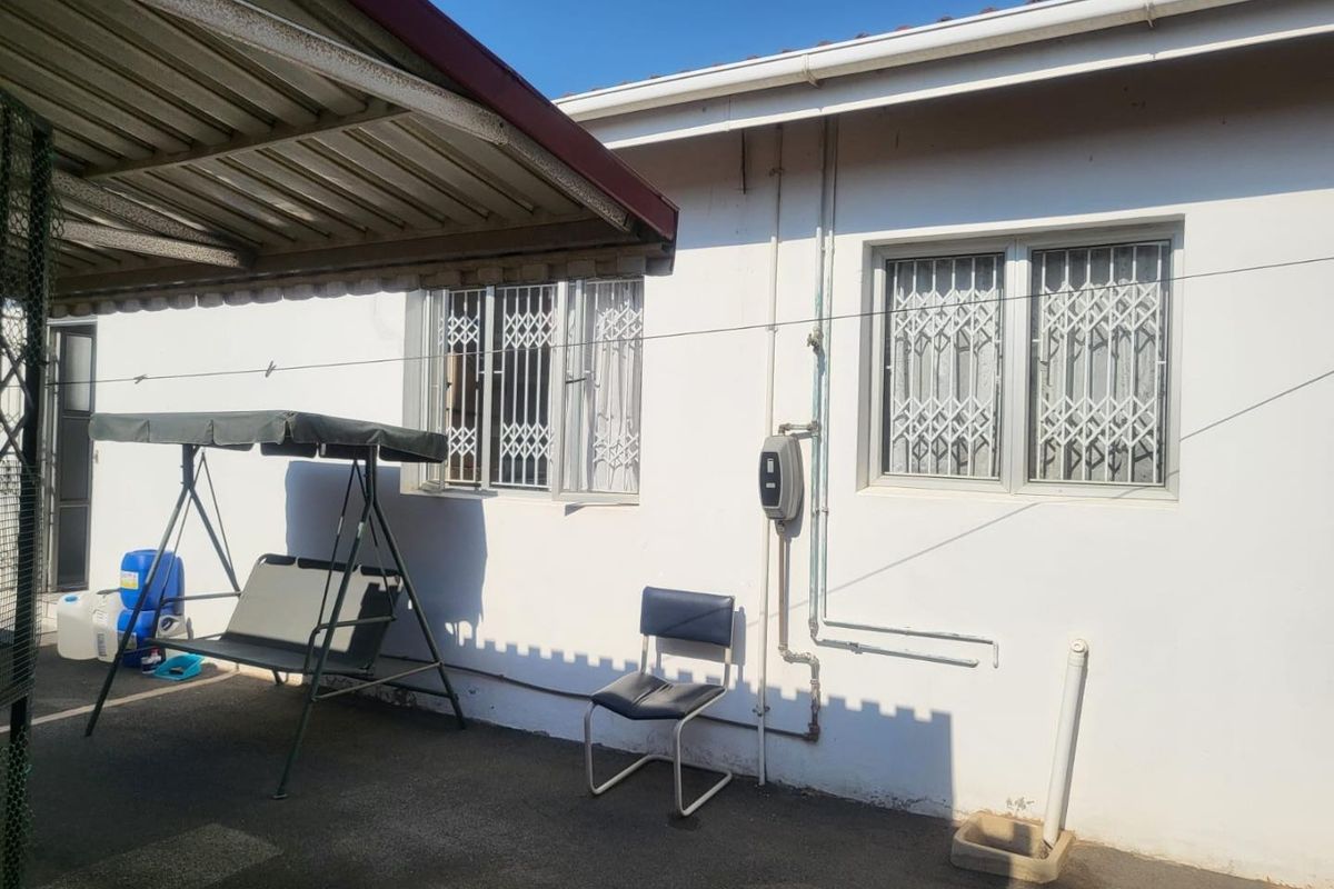 Rear exterior view of the property featuring a paved area, security gates on windows, and a metal roof structure.