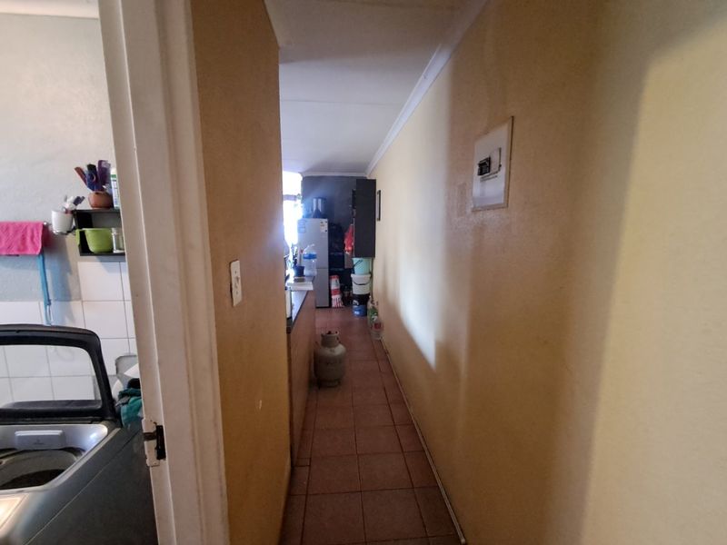 A narrow hallway with tiled flooring and coving, leading towards the kitchen area, featuring a wall-mounted electrical distribution board.