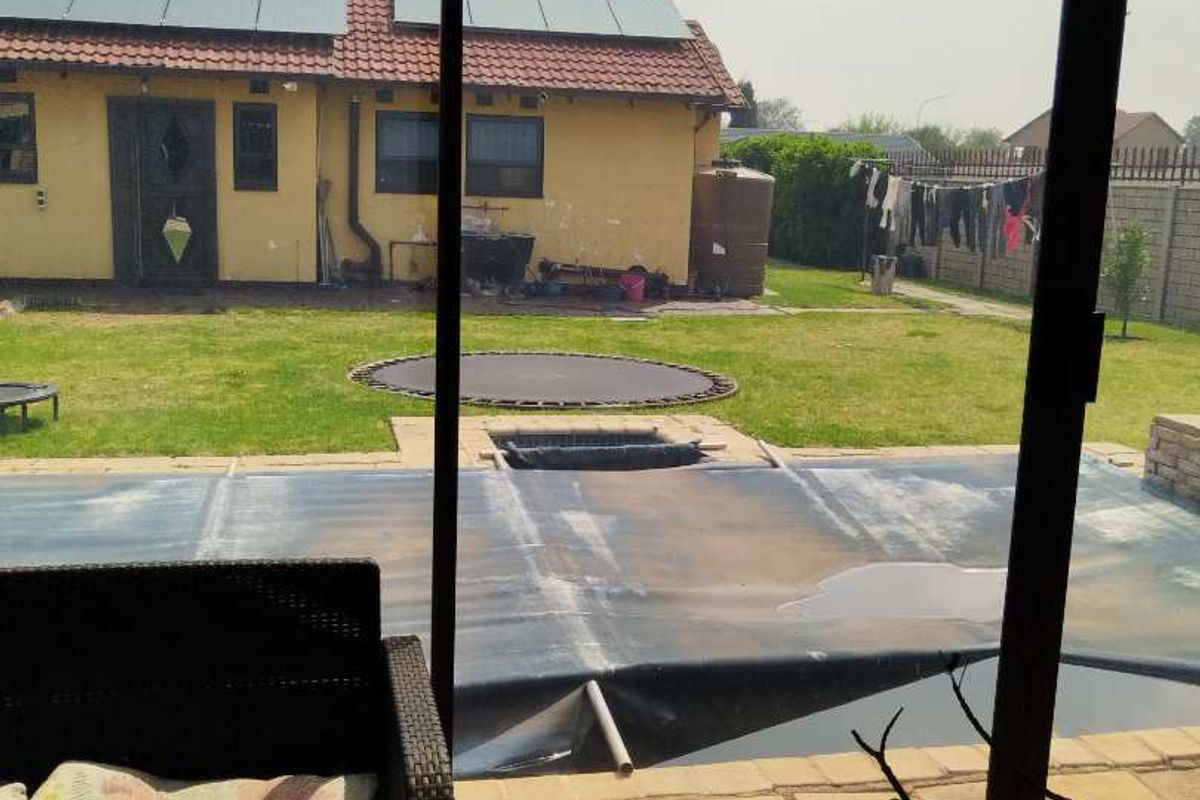 Rear view of the property featuring a paved patio, a swimming pool with a cover, a lawn, and a house with solar panels.